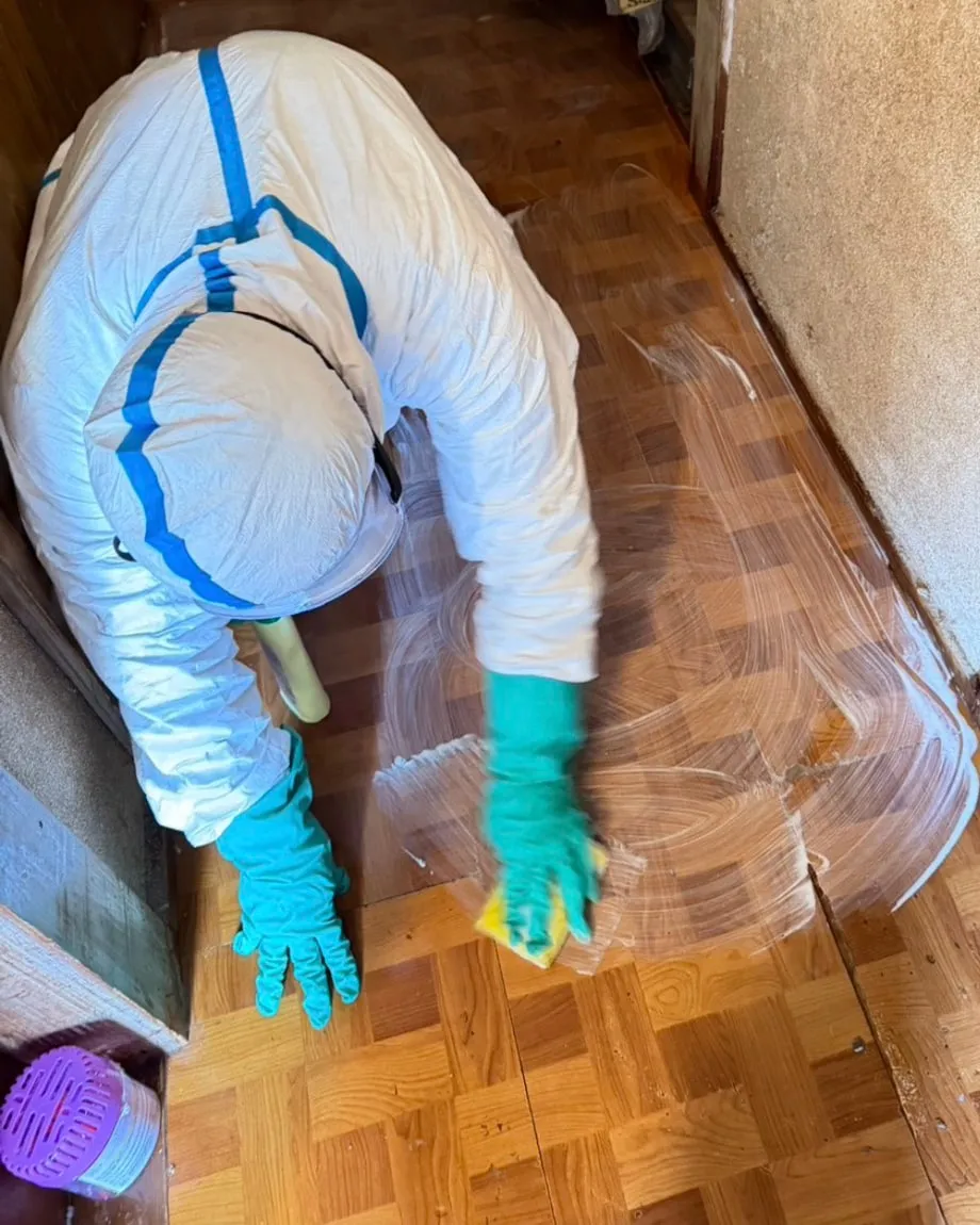 防護服を着た当社スタッフが、床をスポンジで清掃しているところ